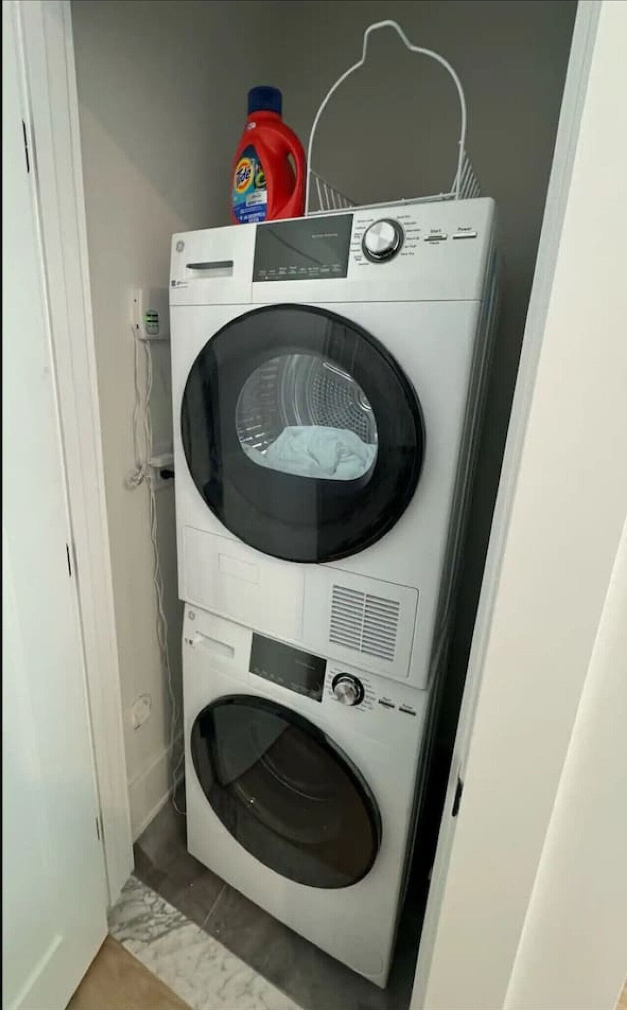 Una lavadora y secadora apiladas en un lavadero pequeño con una puerta a la izquierda.