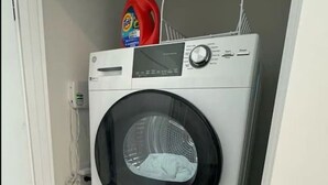 Un appareil combiné lave-linge et sèche-linge, de type «empilable», installé dans une petite buanderie, avec une porte sur le côté gauche.