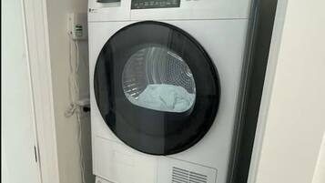 Una lavadora y secadora apiladas en un lavadero pequeño con una puerta a la izquierda.