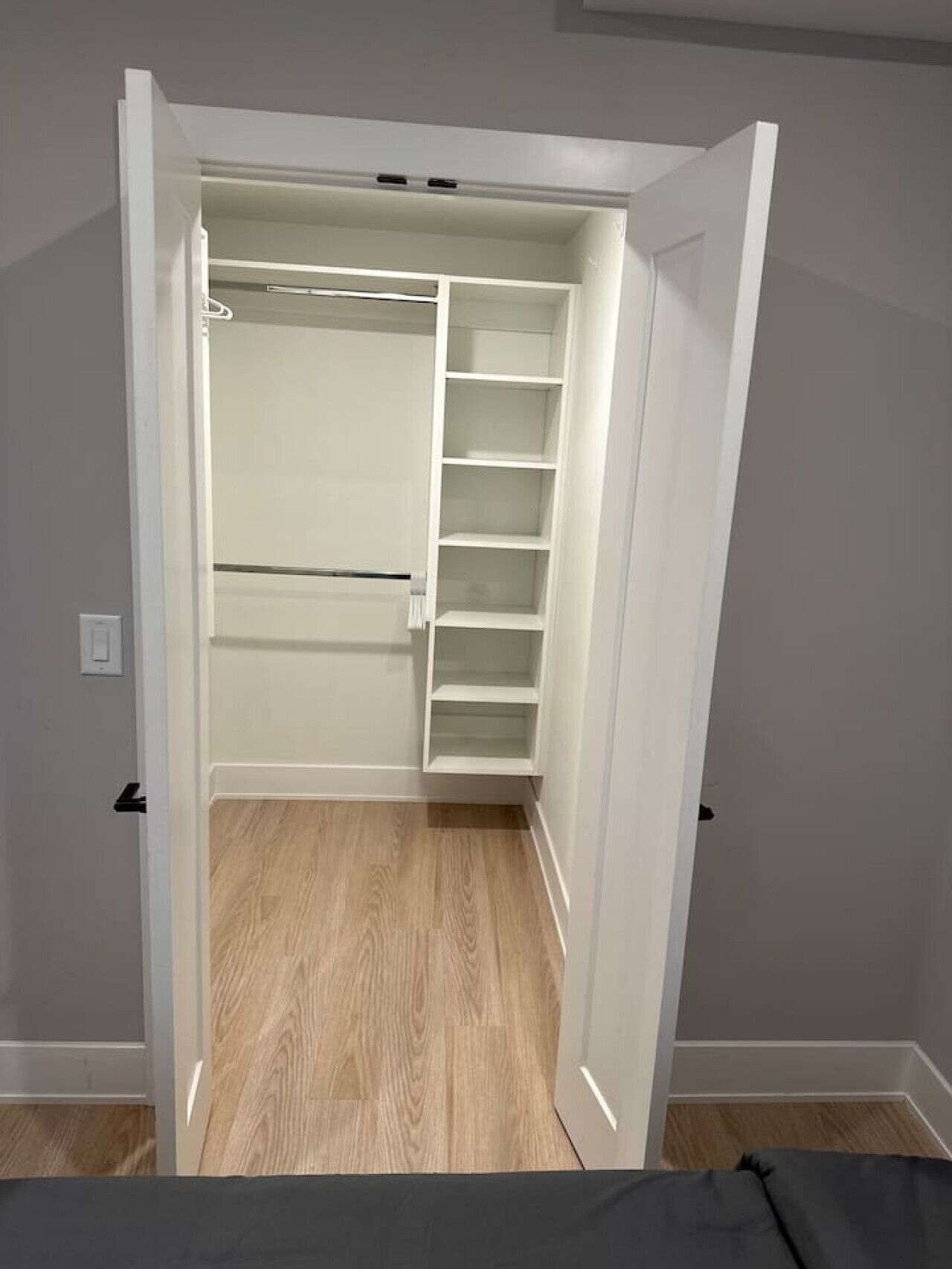 A walk-in closet with open doors, wooden flooring, and white shelving units.