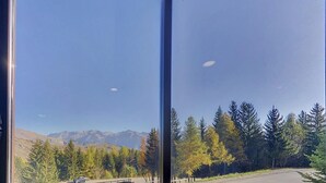 A view through a window with a mountain range in the background, a road, and a forest with autumn-colored trees.