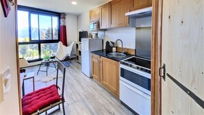 A compact kitchen with wooden cabinets, a built-in oven, and a window overlooking a mountainous landscape.