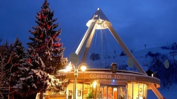A snow-covered building with a conical roof, labeled "CORBIER TOURISME," surrounded by snow-laden trees.