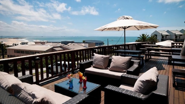 A deck with outdoor furniture, a large umbrella, and a view of the sea and buildings.