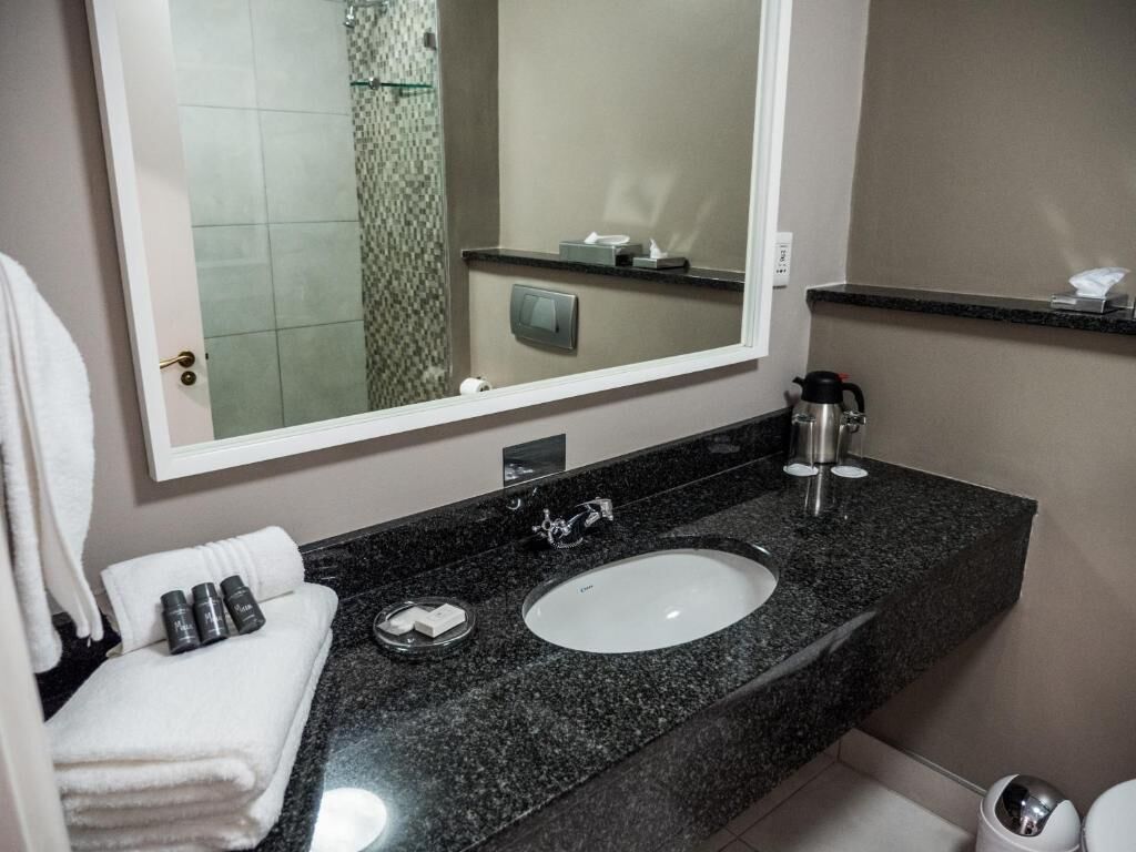 Une salle de bain avec un grand miroir, un lavabo, un porte-serviettes et des toilettes.