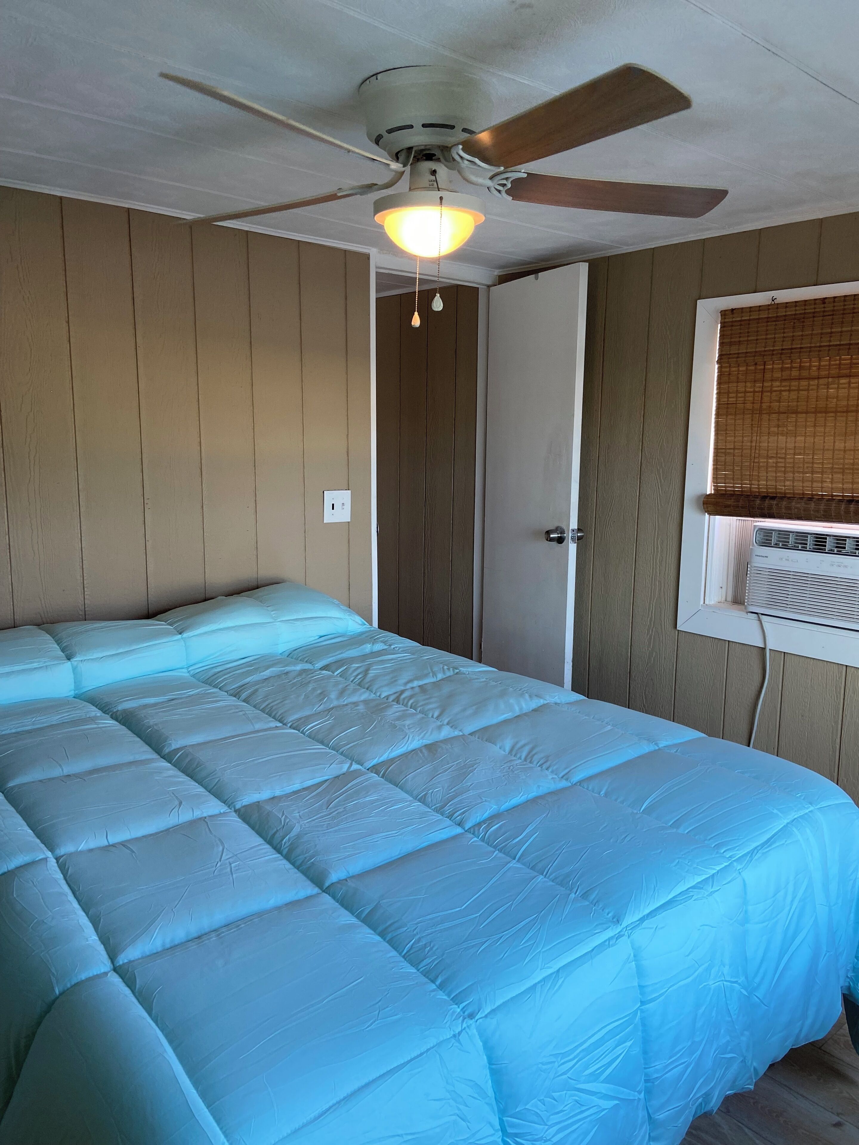 Een slaapkamer met een bed, een plafondventilator, een raam met blinds en een wandairconditioner.