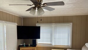 A living room with a ceiling fan, two wicker side tables, a flat-screen TV, and a beige sofa.
