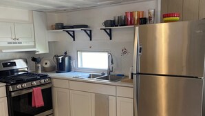 A modern kitchen with white cabinets, a stainless steel refrigerator, a gas stove, and a window above the sink.