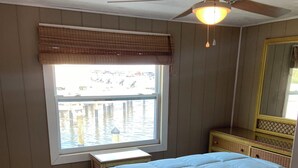A bedroom with a bed, a window with blinds, a ceiling fan, and a wooden floor.