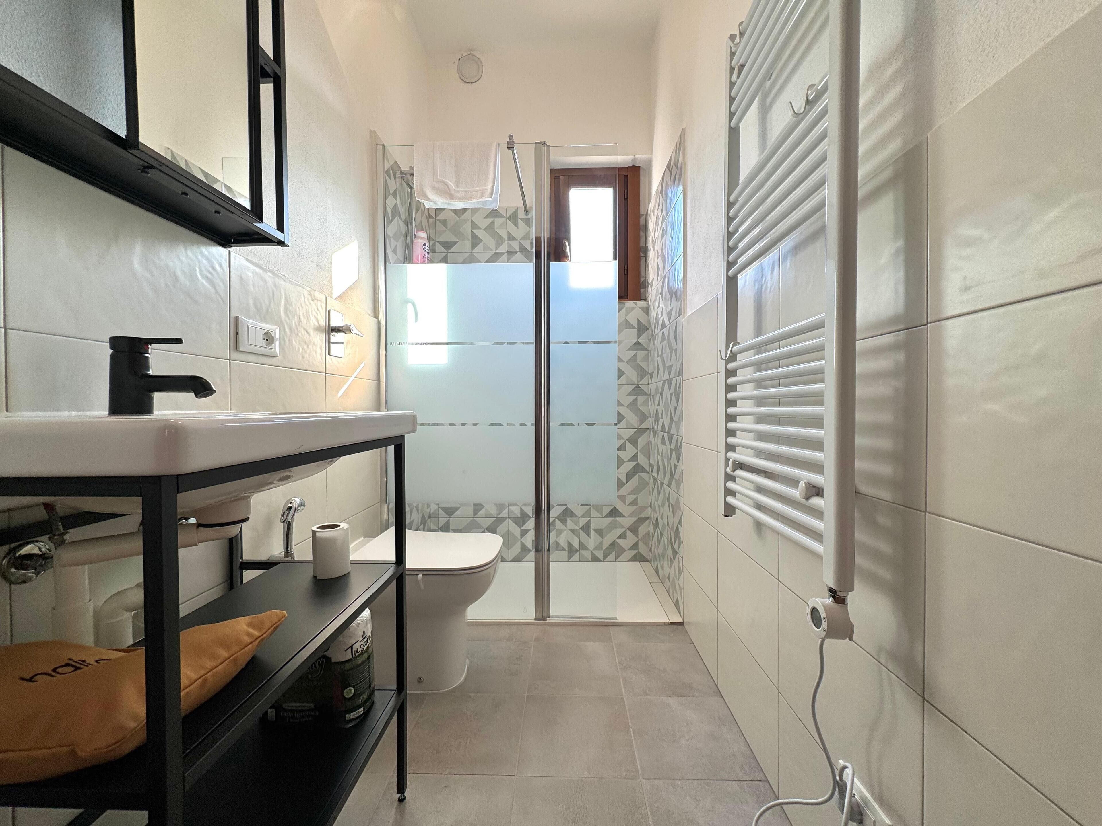A bathroom with a toilet, a sink, a towel rack, and a shower area.