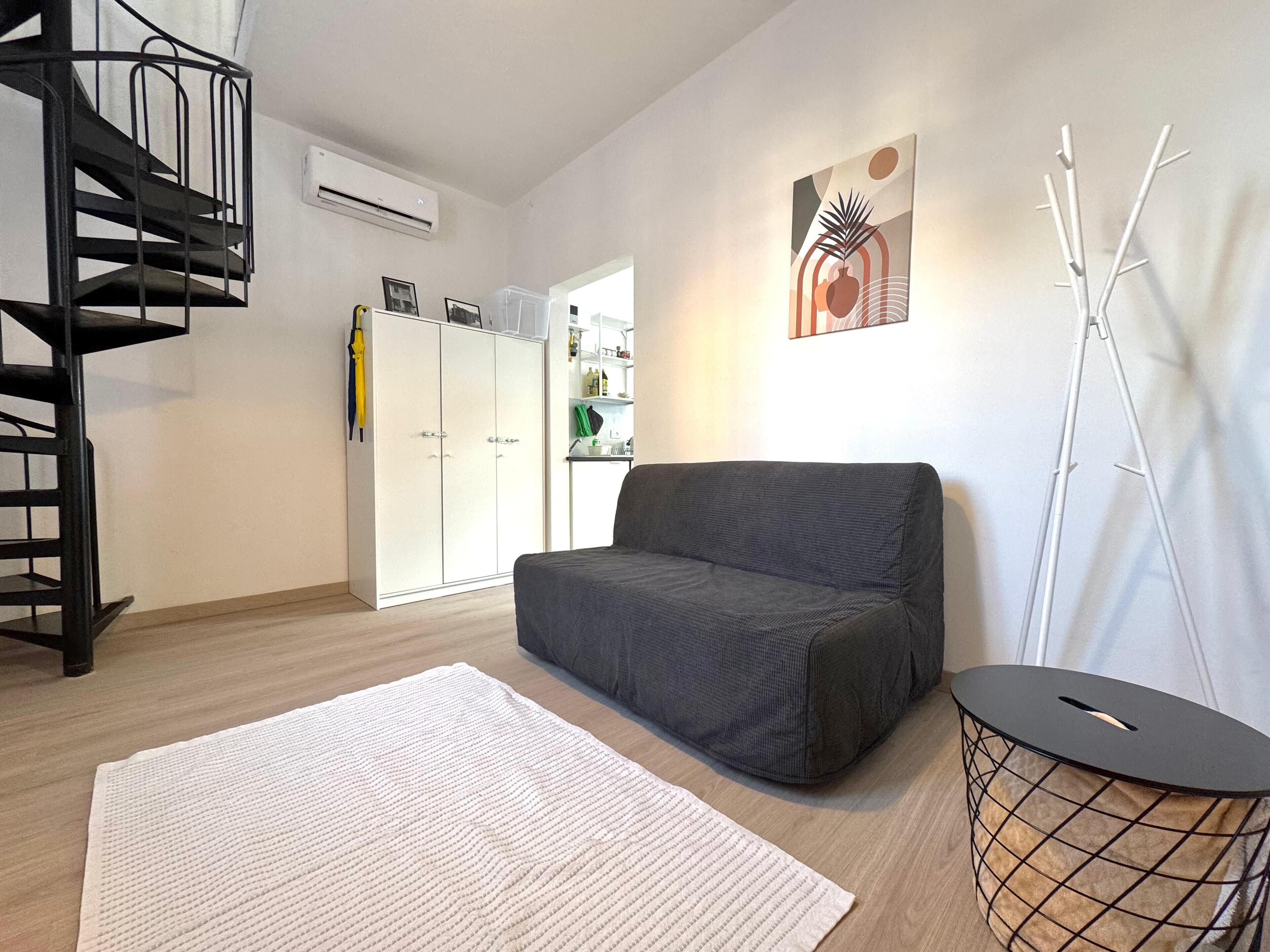 A modern living room with a grey sofa, a white rug, a black floor lamp, and a white wardrobe.