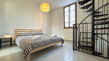 Een slaapkamer met een bed, een nachtkastje, een hanglamp, een raam en een wenteltrap.