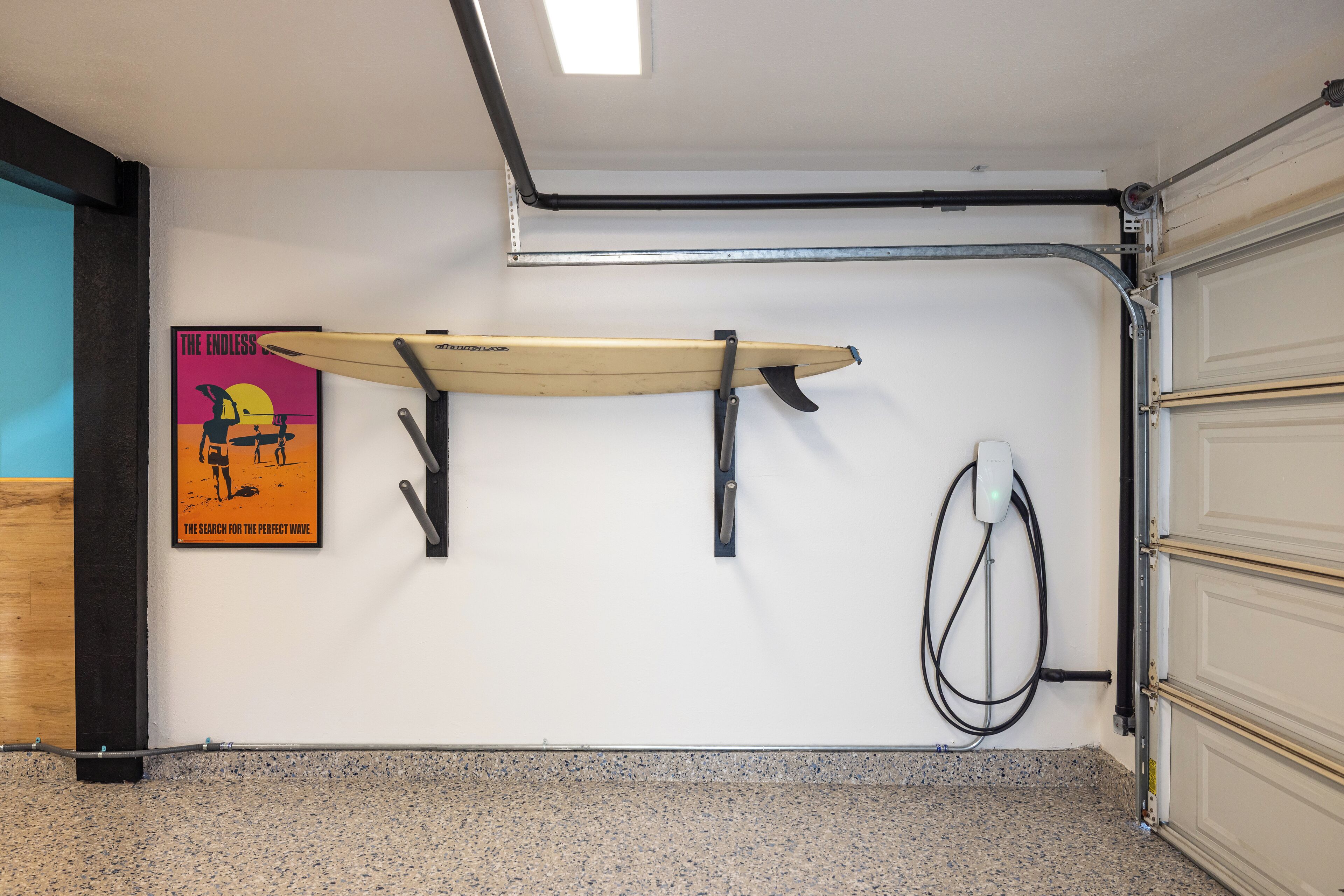 A garage with a surfboard mounted on the wall, a poster, and a power outlet.