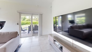 Una sala de estar moderna con una televisión de pantalla plana, un sofá y un ventanal corredero que da a un patio exterior con mobiliario.