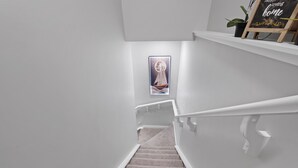 Un escalier avec une rampe, des marches recouvertes de moquette et un cadre photo fixé au mur.