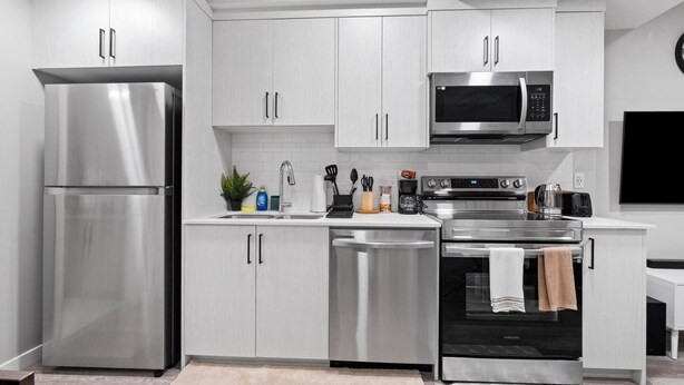 Une cuisine moderne dotée d’appareils électroménagers en acier inoxydable, de meubles blancs et d’un four encastré.