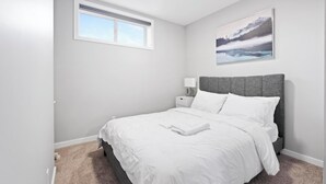 Une chambre à coucher avec un lit, une table de chevet, une lampe, une fenêtre et un tableau accroché au mur.