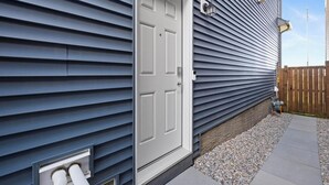 Une maison avec une porte d’entrée blanche, des évents extérieurs et une clôture en bois.