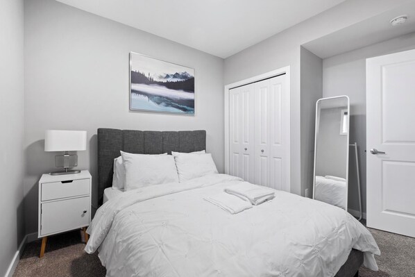 Une chambre à coucher avec un lit, une table de chevet avec une lampe, une armoire et un tableau encadré accroché au mur.