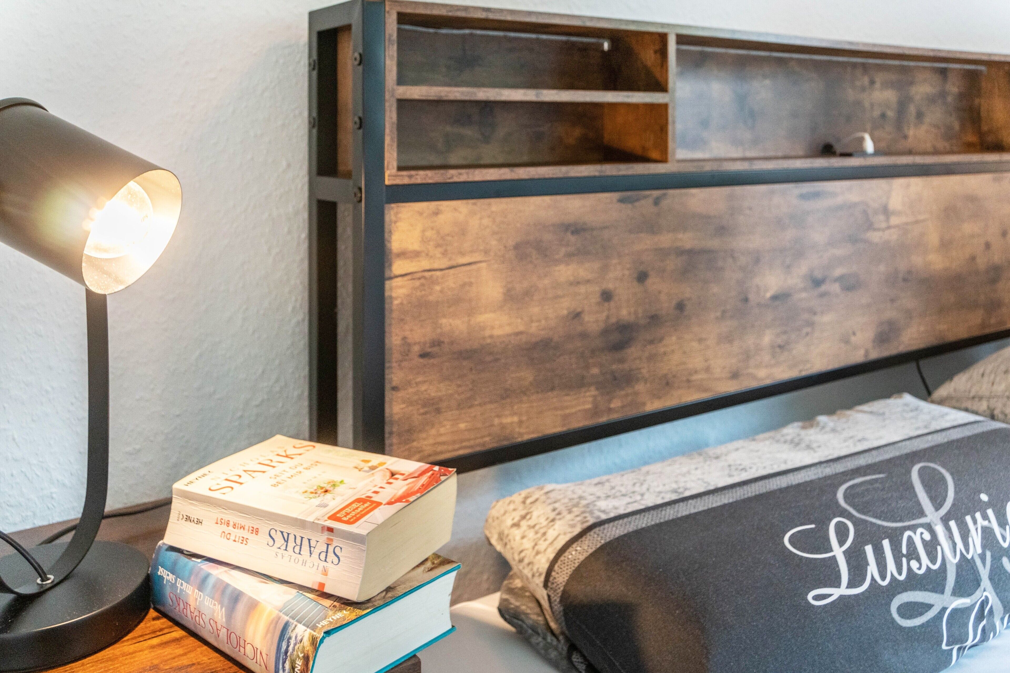 A bed with a pillow labeled 'Lucy,' a bedside table with a lamp, and a stack of books.