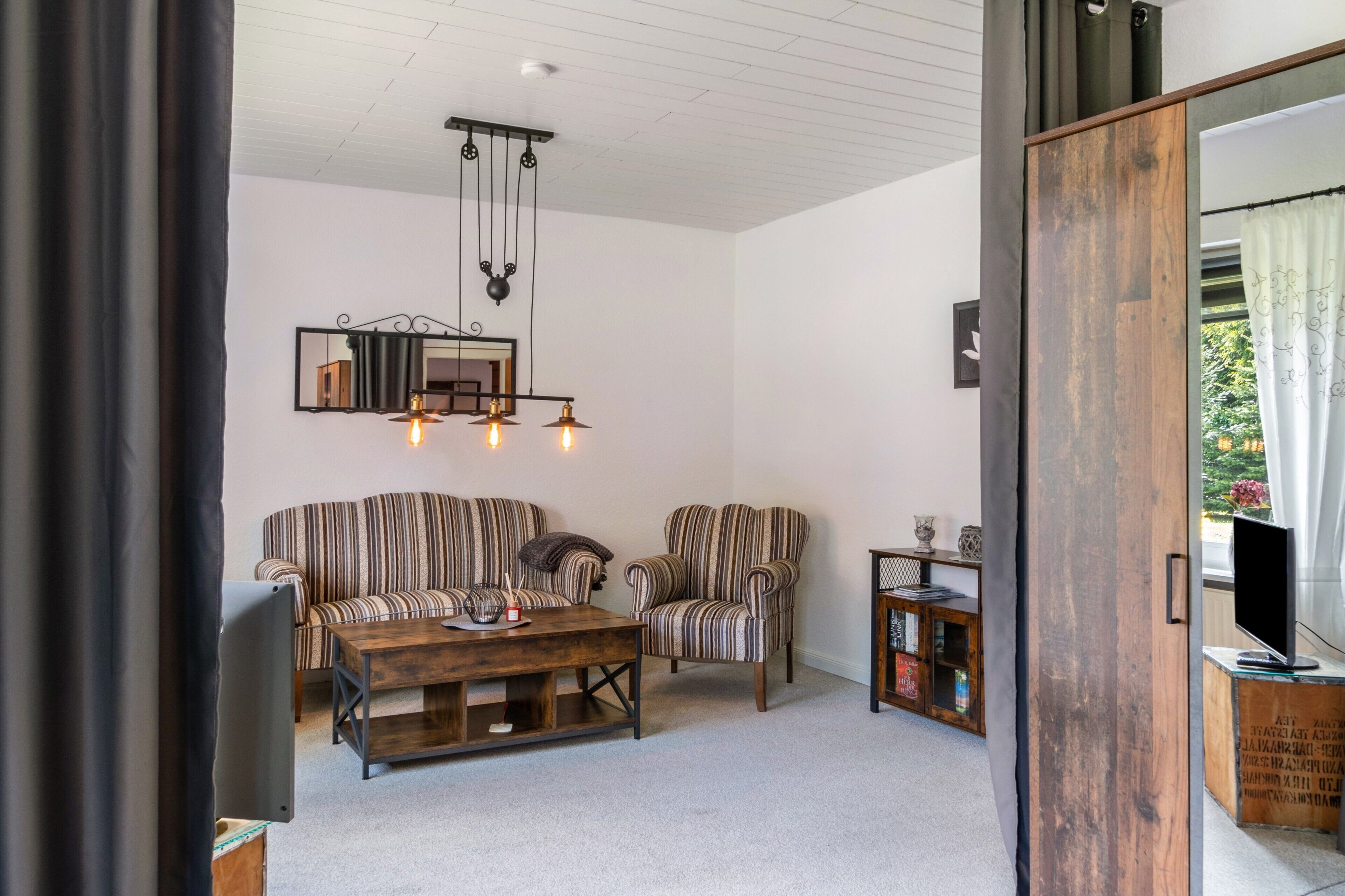 Una sala de estar con sofás a rayas, una mesa de centro de madera, un colgador de luz y un televisor.