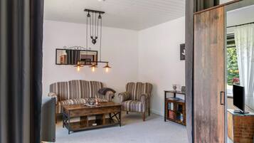 Una sala de estar con sofás a rayas, una mesa de centro de madera, un colgador de luz y un televisor.