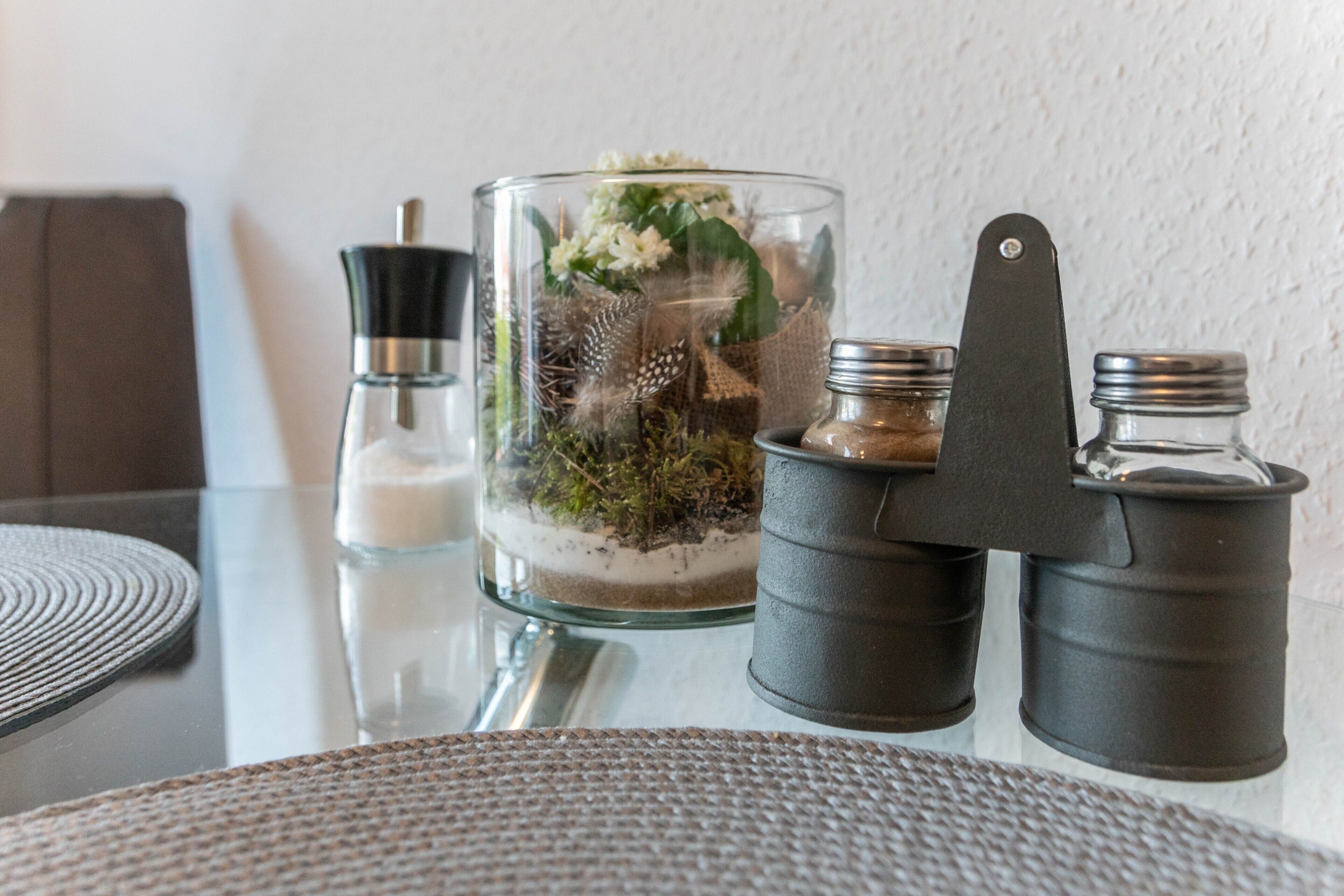A glass container with a plant and a metal object on a table.