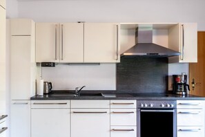Una cocina moderna con gabinetes blancos, una campana de acero inoxidable y un horno empotrado.