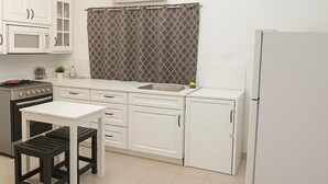 A modern kitchen with white cabinetry, a gas stove, a microwave, a sink, and a refrigerator. - Barmel Apartments (Coxen Hole)