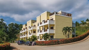 A multi-story hotel with balconies, a curved driveway, and landscaped areas with red flowers. - Barmel Apartments (Coxen Hole)