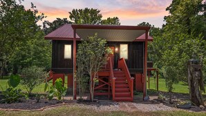 Una cabaña rústica con fachada roja, un porche cubierto y una escalera que lleva a la entrada.