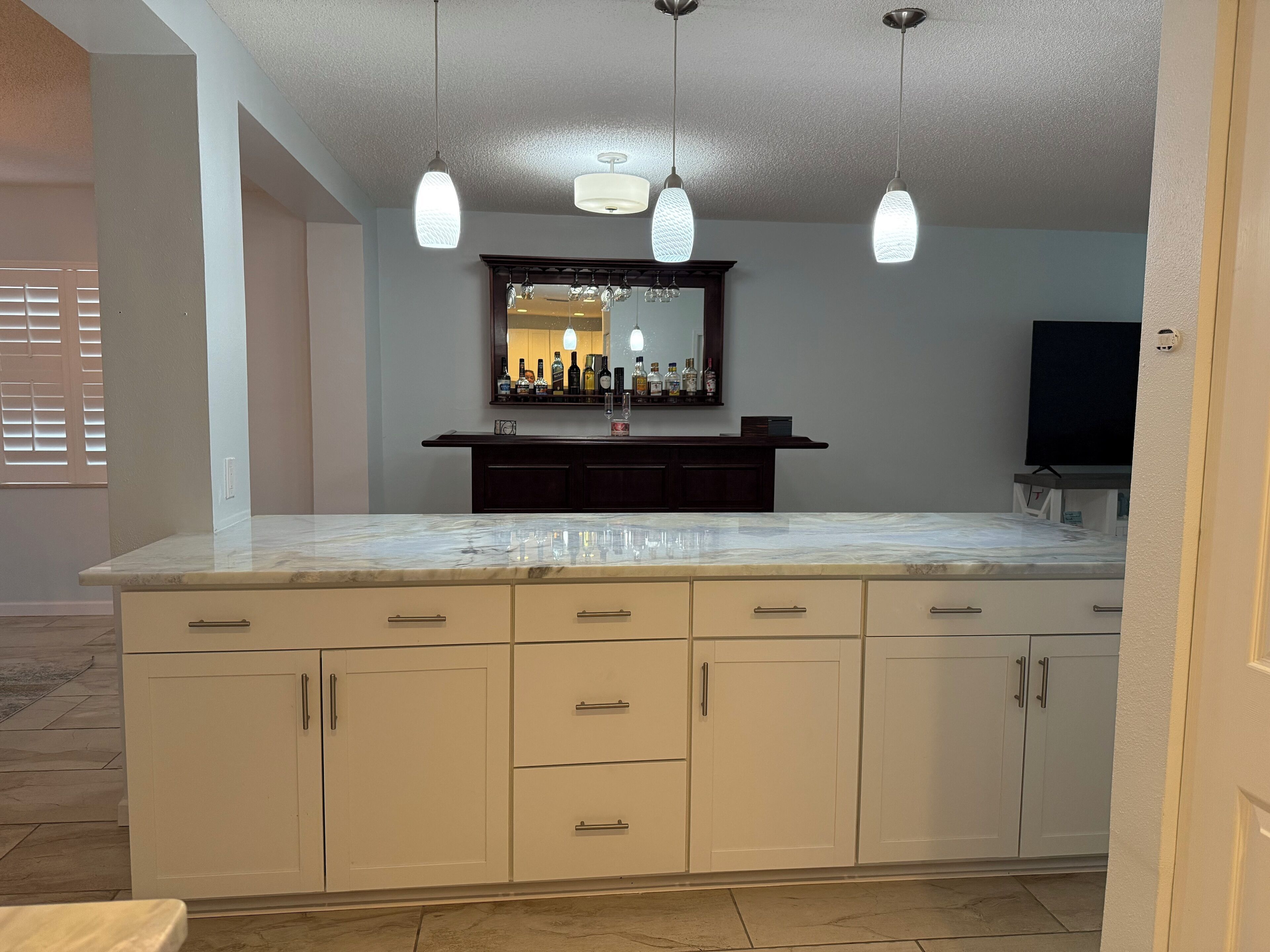 A kitchen with a marble countertop, white cabinets, and pendant lights.
