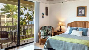 Habitación de hotel con cama, una silla, una mesa y un balcón con palmeras.
