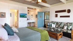 Un dormitorio con una cama, una manta verde, una mesita de madera y un ventilador de techo.