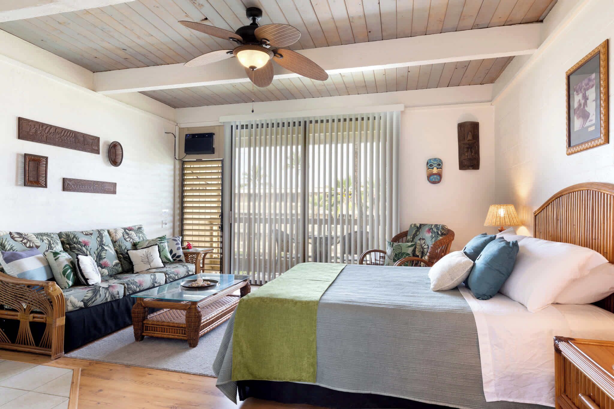 A room with a bed, a sofa, a dining table, and a ceiling fan.