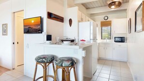 Una cocina moderna con armarios blancos, una isla central con taburetes, un televisor montado en la pared y un reloj de pared.