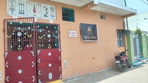 A building with a red gate, a motorcycle parked outside, and a sign with text. - Baikuntha Dham Bhakta Niwas (Puri)