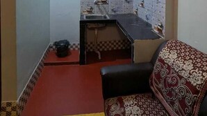 A compact room with a kitchenette, a sofa, and a patterned rug. - Baikuntha Dham Bhakta Niwas (Puri)