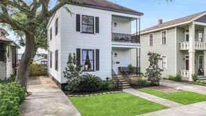 A two-story house with a front porch, a small garden, and a tree in the yard.