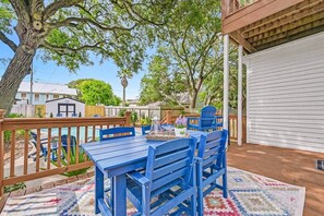 Une terrasse avec une plateforme en bois, une table bleue entourée de chaises et une piscine en arrière-plan.