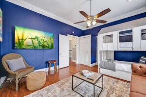 Un salon avec un ventilateur de plafond, un grand tableau, un fauteuil en osier, une table basse et un canapé.