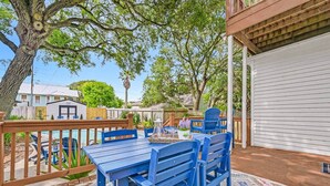 A patio with a wooden deck, a blue table with chairs, and a pool in the background.