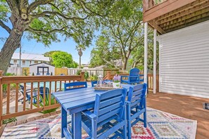 Une terrasse avec une plateforme en bois, une table bleue entourée de chaises et une piscine en arrière-plan.