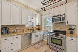 Una cocina con armarios blancos, electrodomésticos de acero inoxidable, horno empotrado y microondas.