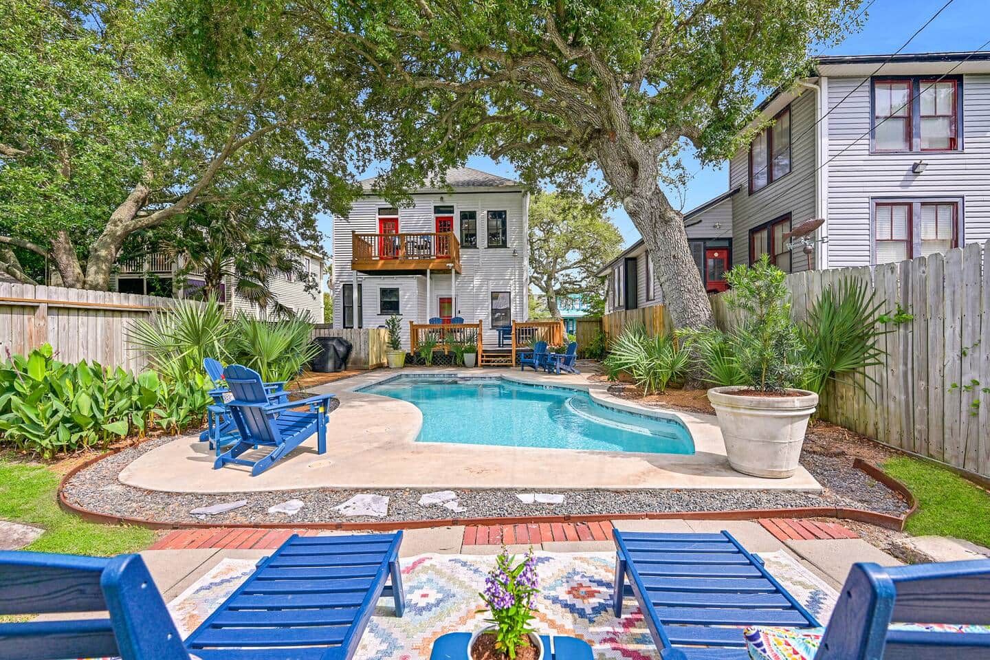 Un jardin avec une piscine, des chaises longues bleues et une terrasse en bois.