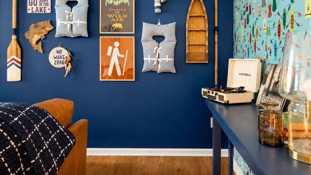 Une pièce avec un mur bleu, un plancher en bois et divers éléments de décoration sur le thème de la navigation, notamment une pagaie, un panneau sur lequel on peut lire « ALLEZ, SAUTEZ DANS LE LAC » et un mur orné d’illustrations maritimes.