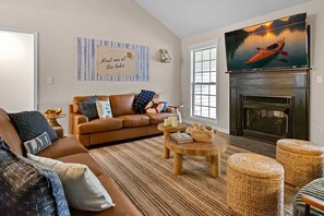 Ein Wohnzimmer mit einem braunen Sofa, einem Kamin, einem Fernseher und einem Bild von einem Kanu auf einem See.