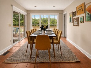 A dining area with a table set for six, surrounded by chairs, with a view of greenery outside through large windows. - Lakefront Home, Hot tub, Fire Pit, Game Room, & Movie Room! (Marion)
