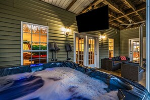 A hot tub with a view of a mountain landscape, a television mounted on the ceiling, and a seating area with wicker furniture.