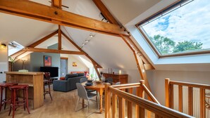 Un loft spacieux avec de hauts plafonds, des poutres apparentes, un coin repas, un salon doté d’un canapé et une grande verrière.